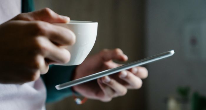 lighter skinned hands holding a mug and tablet